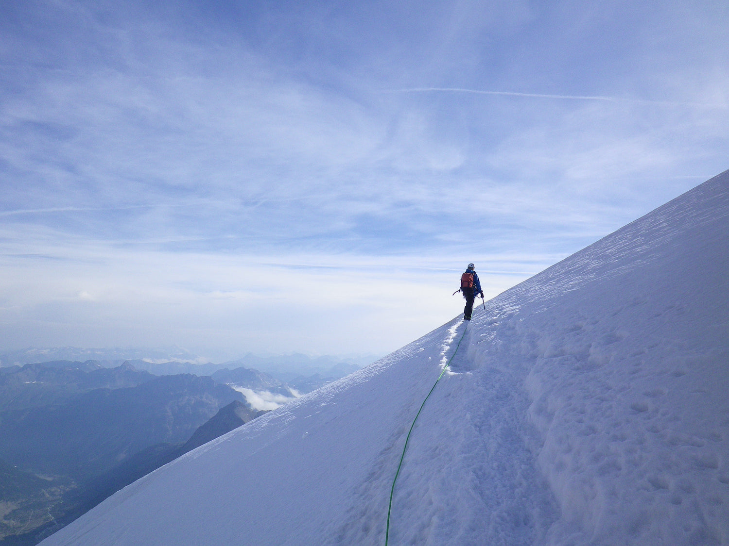 A female Alpinist traverses a snow slope under a cloudy blue sky