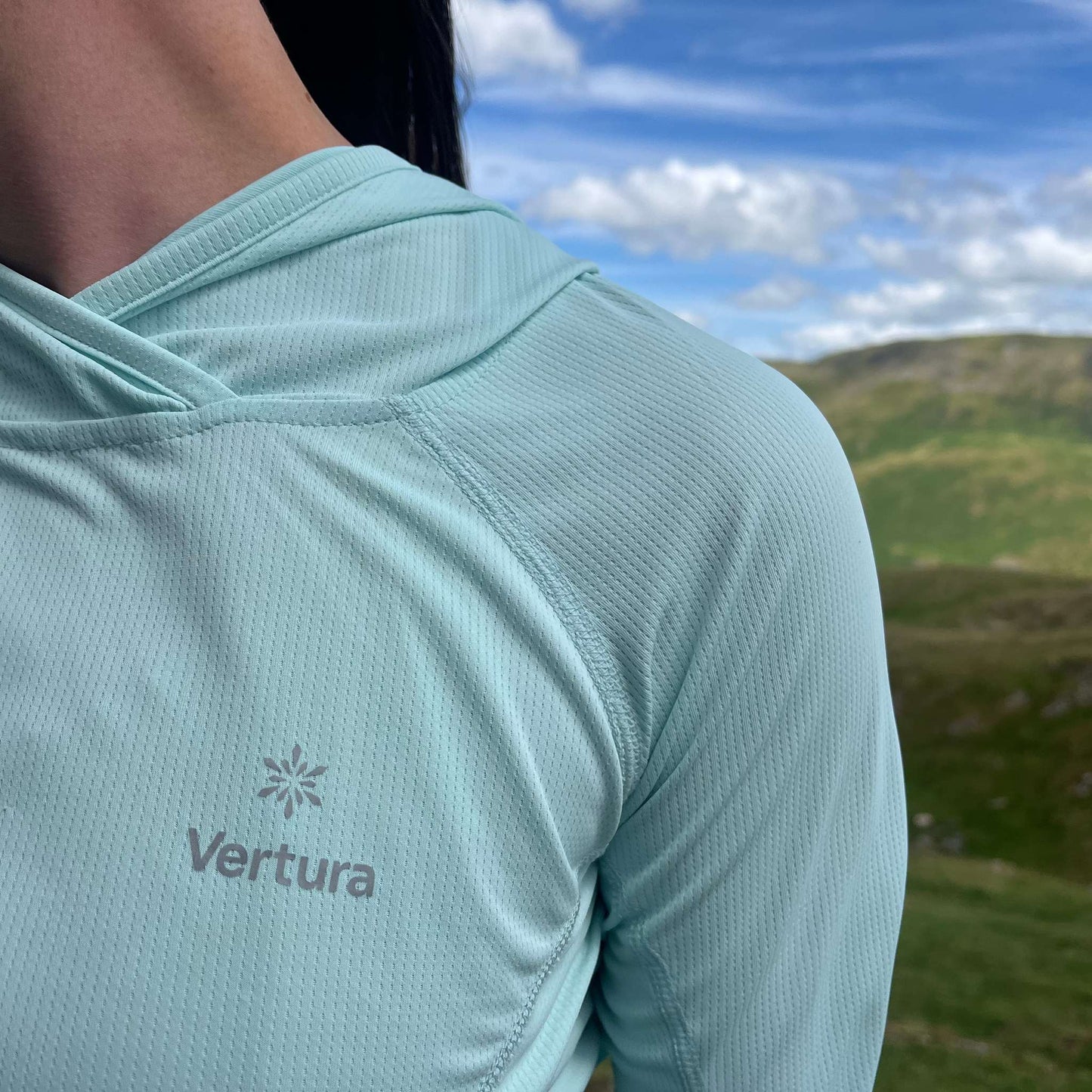Shoulder detail of the Soltera Hoody in glacial green, worn on a hillside